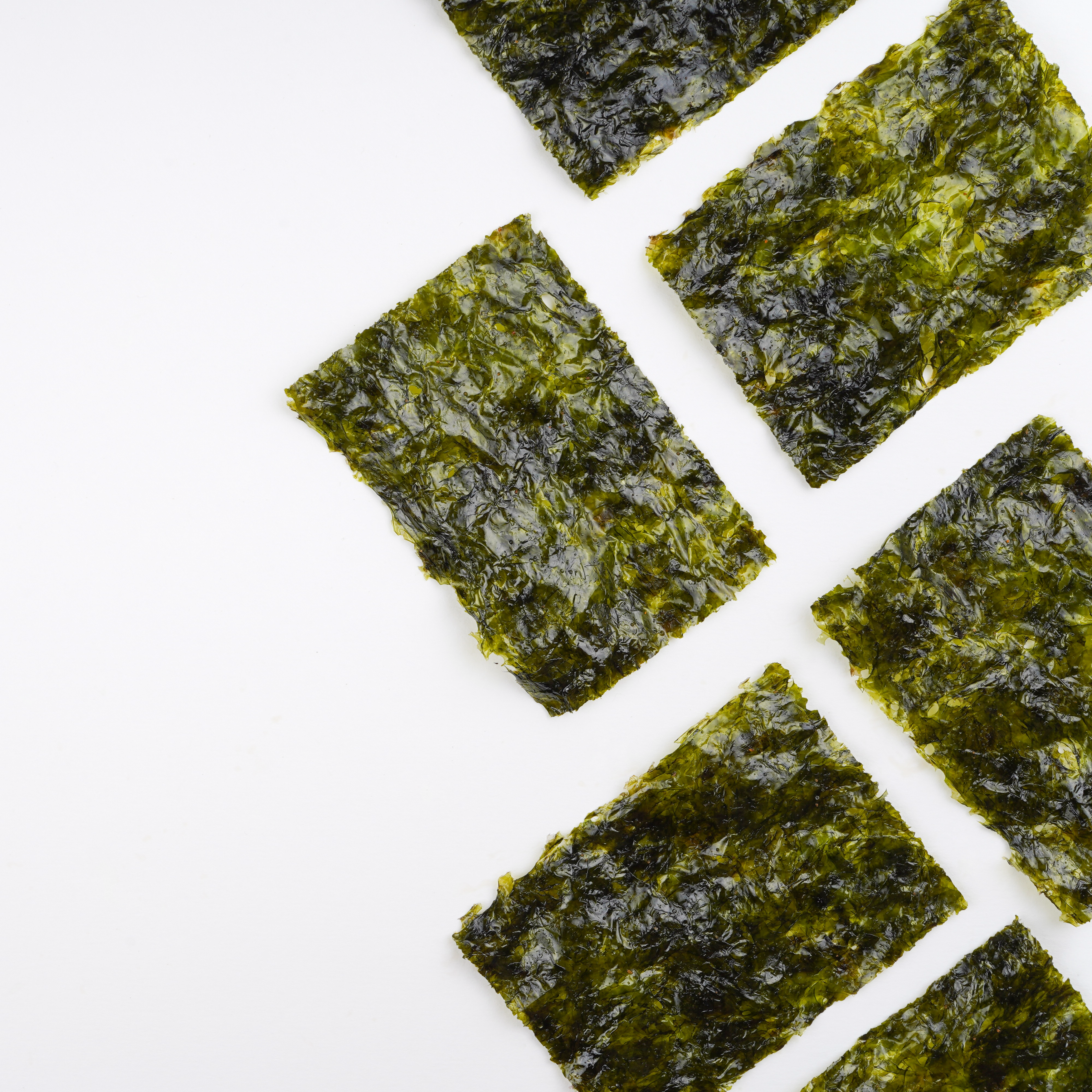 Zes rechthoekige vellen gedroogd zeewier staan in een diagonaal patroon op een witte achtergrond.